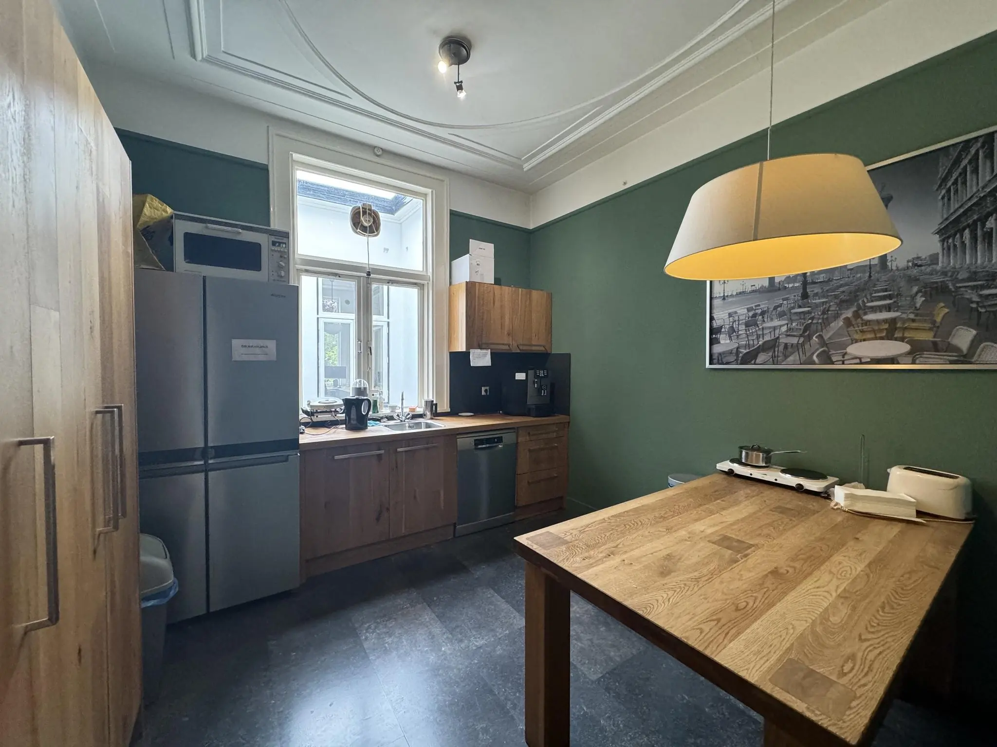 Moderne keuken aan de Dorpsstraat met houten elementen, groene muren en een grote hanglamp boven een houten eettafel.